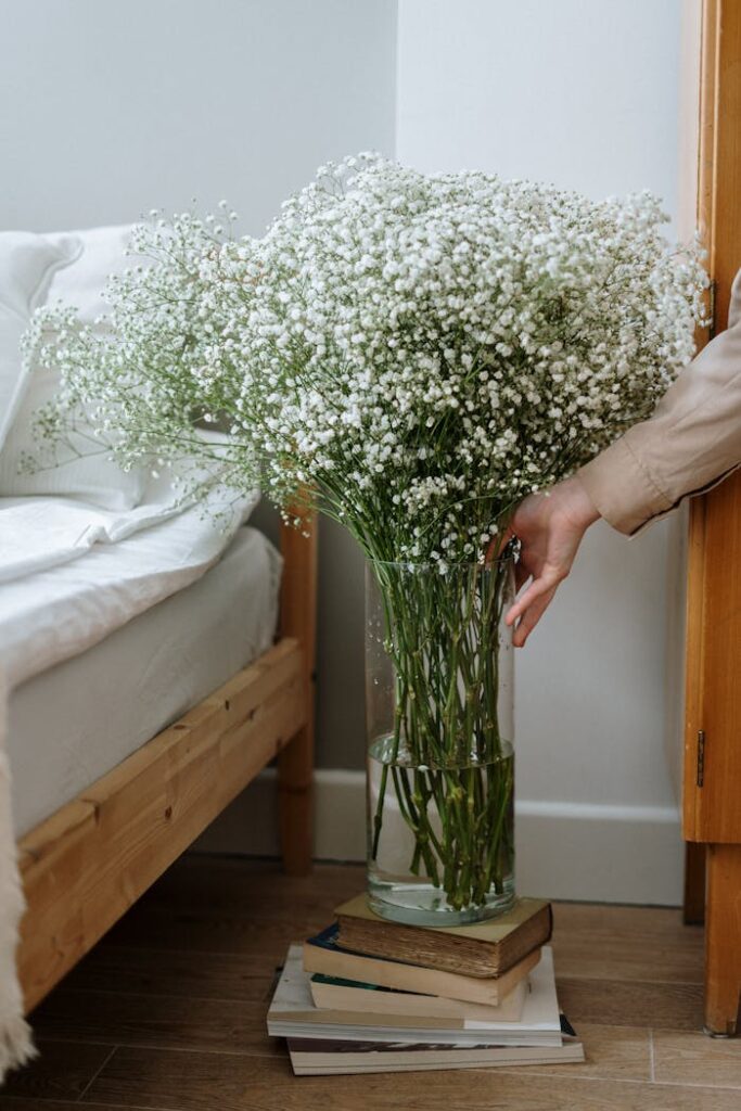 A large gypsophila bouquet in a glass vase adds elegance to a cozy bedroom setting.