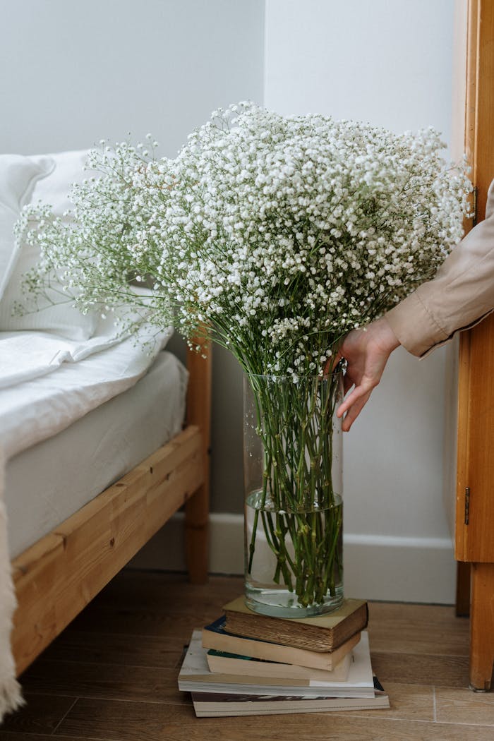 A large gypsophila bouquet in a glass vase adds elegance to a cozy bedroom setting.